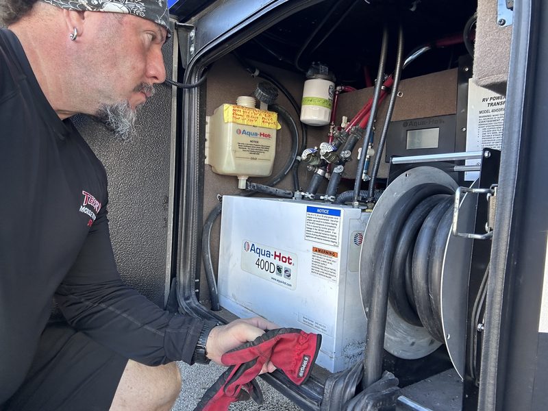 TekRV technician at the open service bay of an Aqua-Hot 400D hydronic heater in an Entegra diesel coach at Las Vegas Motor Speedway