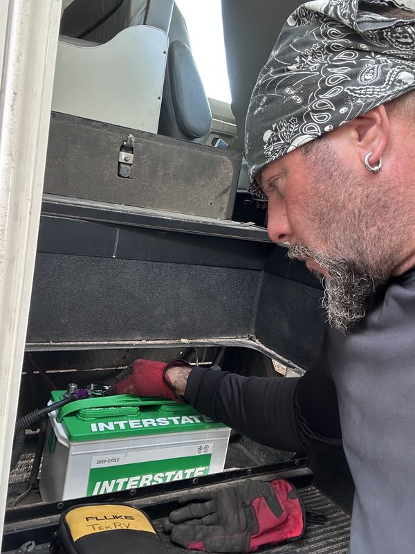 TekRV technician Steve fitting a new Interstate deep-cycle battery in the battery bay of an RV during a Las Vegas service call