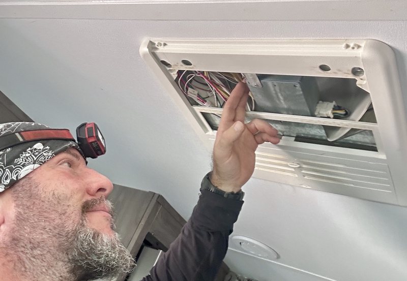 TekRV technician working inside the ceiling air distribution box of an RV rooftop air conditioner during a Las Vegas service call