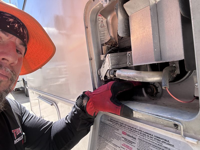TekRV technician servicing a Suburban water heater through the exterior access door of a Coachmen Class C motorhome in Las Vegas